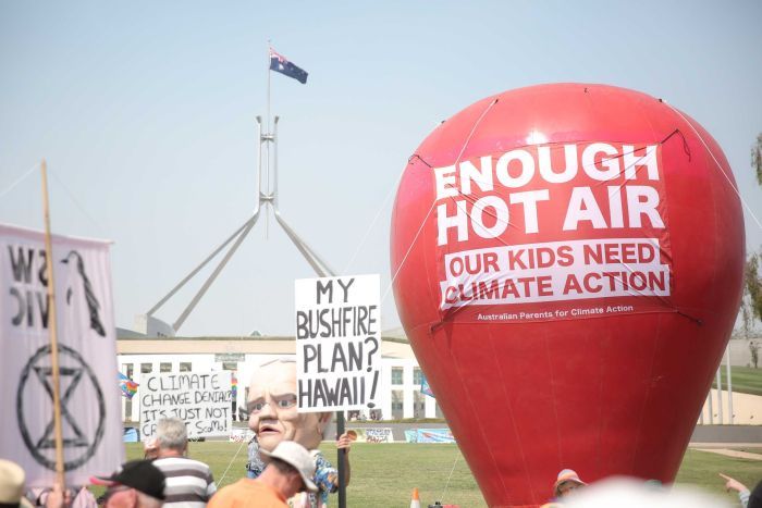 A large red balloon dominates the shot, with a banner on it saying "enough hot air", in front of Parliament House.